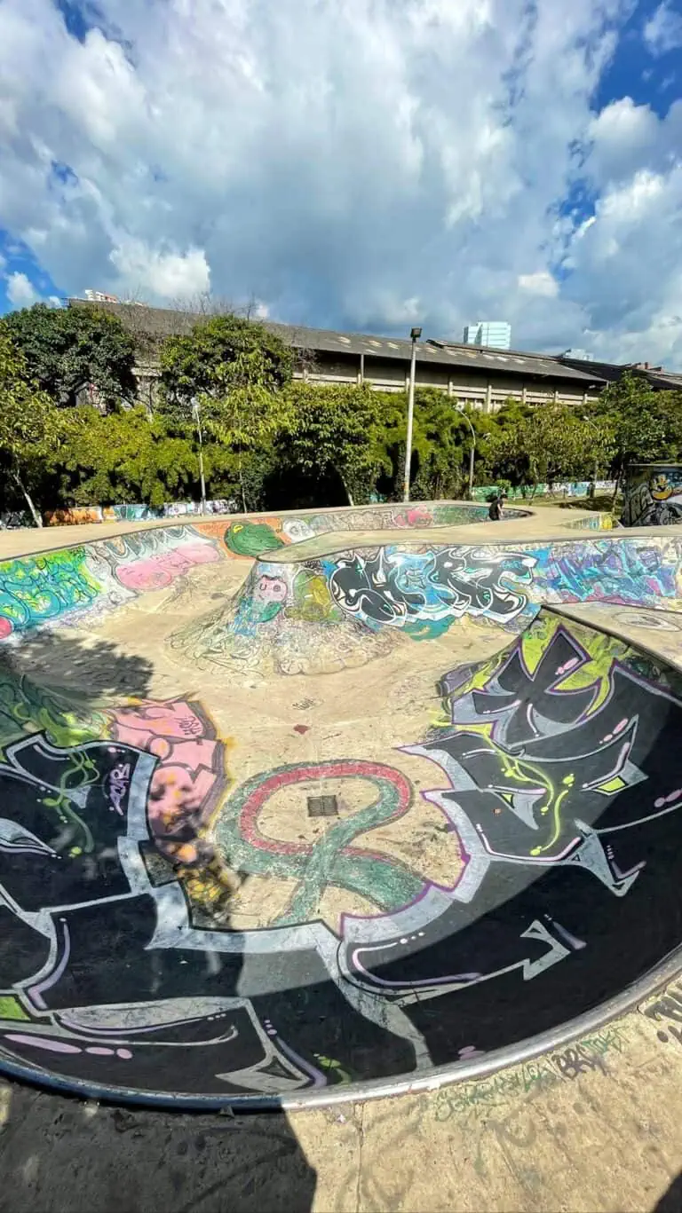 Skatepark couvert de graffitis dans un parc urbain, ciel bleu avec nuages ​​et arbres verts en arrière-plan, espace récréatif pour le skateboard et la culture urbaine à Bogotá, Colombie.