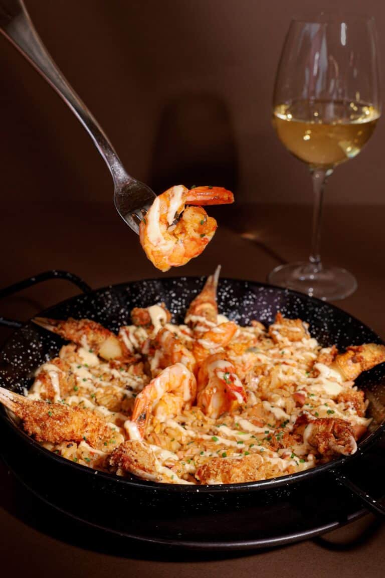 Sabrosa paella de mariscos con gambas y calamares acompañada de una copa de vino blanco en un entorno elegante. Perfecta para eventos y celebraciones en Colombia.