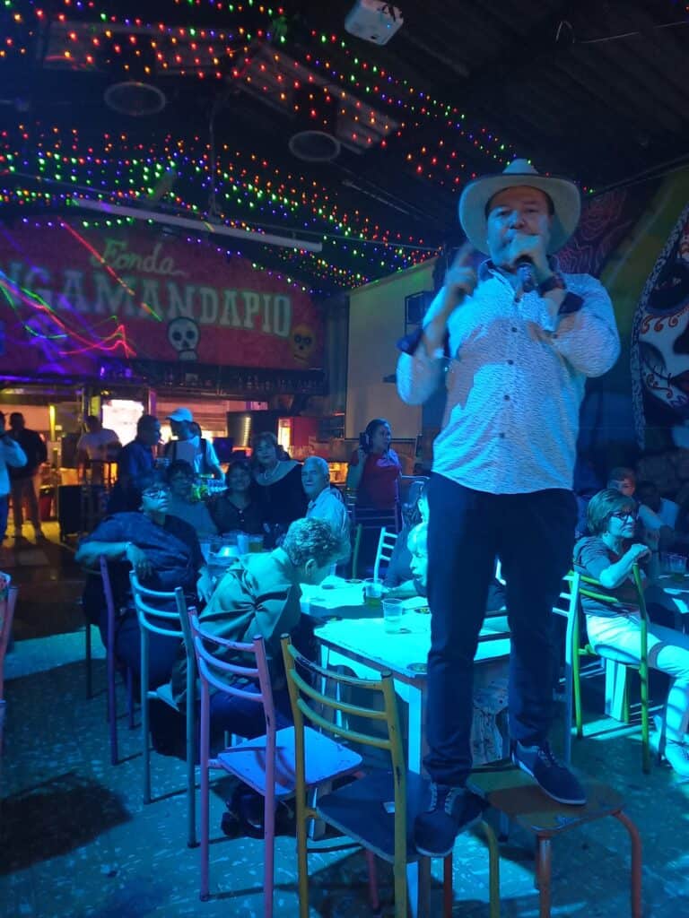 Fiesta en un ambiente colorido con luces decorativas, show en vivo y público disfrutando de música en un evento social.