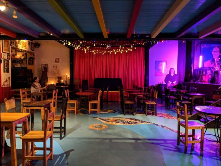 Eventario-concierto-en-vivo-entertainment-diversión-eventos-para-adultos-arte-musical-ambiente-íntimo-y-cómodo,Preesencia de artistas en escenario, ambiente con luces cálidas y decoraciones artísticas, escena de evento musical en espacio con ambiente acogedor y decoración artística, escenario para conciertos en un espacio interior con ambiente relajado y decoración bohemia.