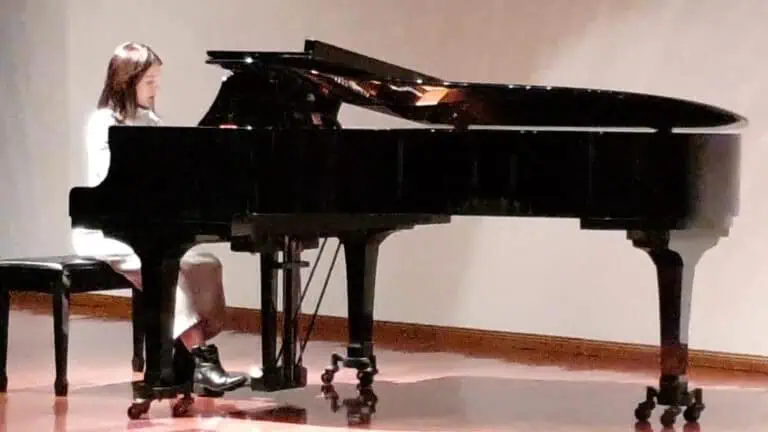Weite Ansicht eines jungen Pianisten, der auf einer Bühne auf einem schwarzen Flügel spielt und eine elegante und künstlerische Atmosphäre für kulturelle und musikalische Veranstaltungen schafft.