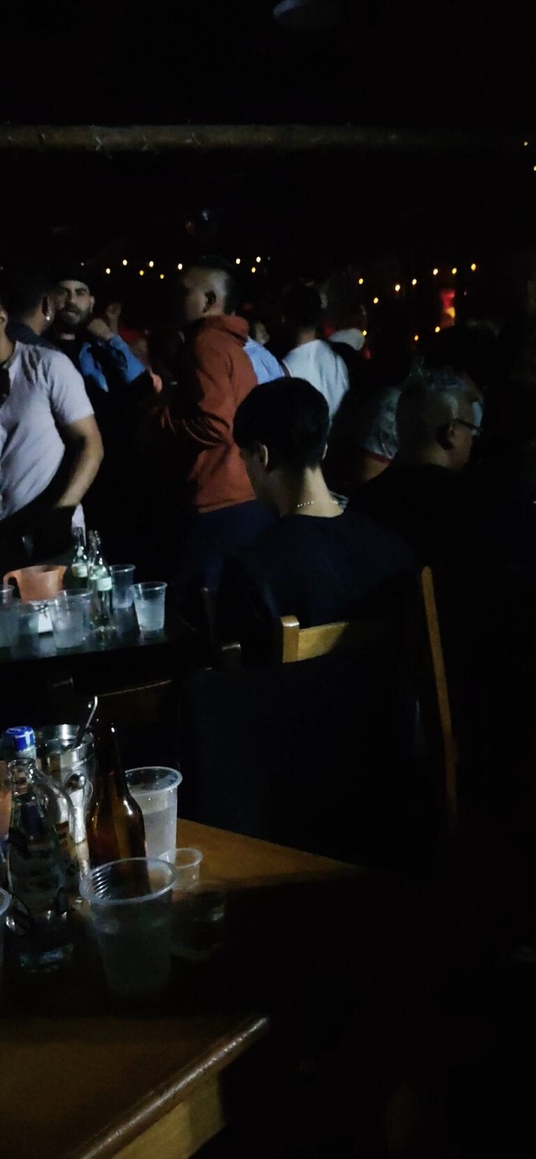 Bajo iluminación en un evento social con personas disfrutando, mesas con bebidas y ambiente festivo en un lugar de eventos en Colombia.