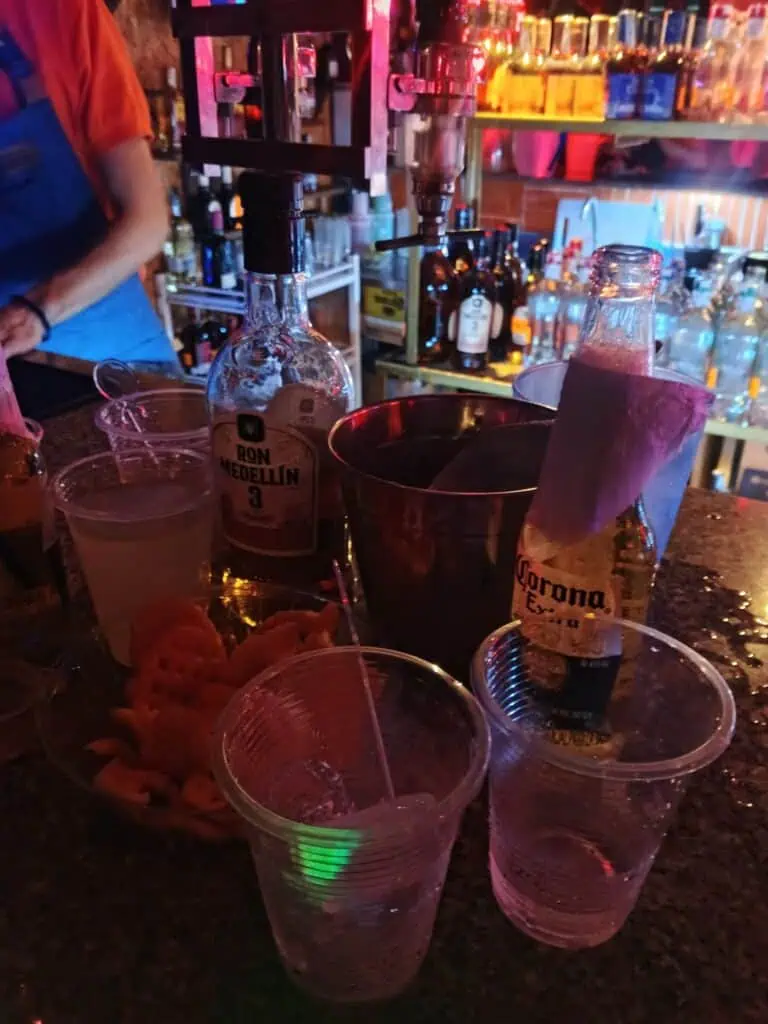 Ron Medellín und Corona an einer Bar mit Getränken und Eis, eine Party- und Feieratmosphäre an einem Ort mit lebendiger Beleuchtung und Dekoration mit Schnapsflaschen und Gläsern.