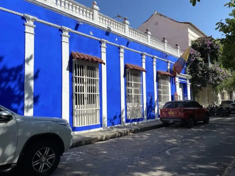 阳光明媚的一天，波哥大一座历史建筑的蓝白相间外墙，周围停放着车辆，树木繁花盛开，是举办文化和旅游活动的理想场所。