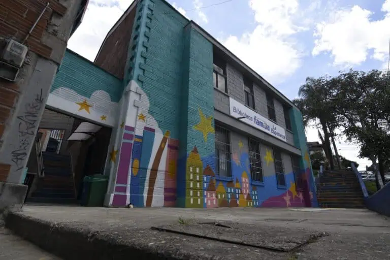 Fresque colorée sur la façade de la bibliothèque familiale La Esperanza, dans une communauté colombienne. La peinture représente un paysage urbain avec des étoiles et des maisons, promouvant la communauté et la culture.