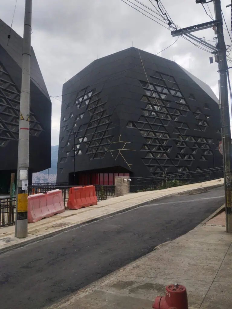 Un bâtiment noir moderne au design géométrique et aux fenêtres en forme de losange, situé dans une zone urbaine avec des lignes électriques et des panneaux de signalisation, représente l'innovation et l'architecture contemporaine.