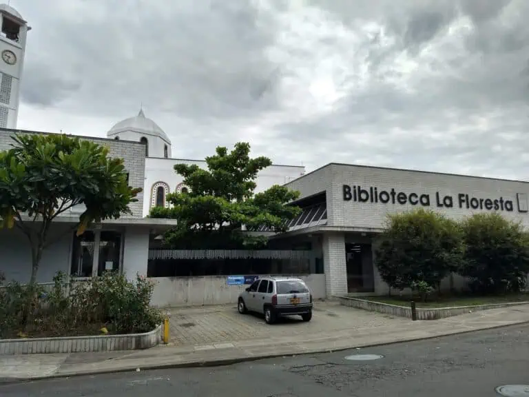 Die Bibliothek La Floresta an einem bewölkten Tag, mit Bäumen und einem vor dem Gebäude geparkten Auto, in einem leicht zugänglichen Stadtgebiet.