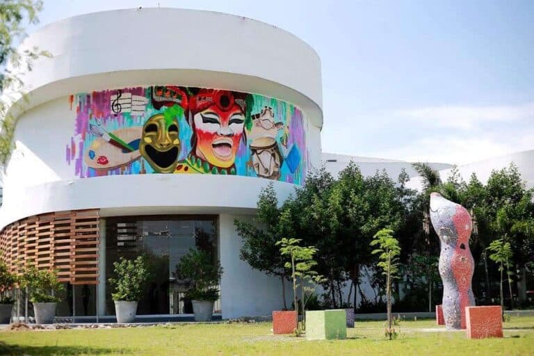 Colorido mural artístico en fachada de edificio moderno en Medellín, con esculturas y áreas verdes, ideal para eventos y actividades culturales.