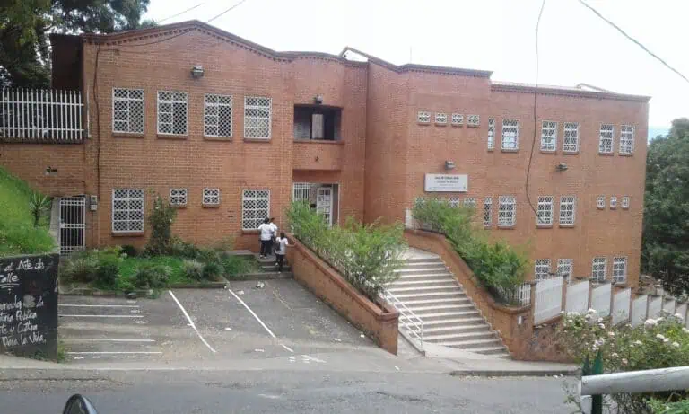 Un bâtiment culturel local en construction avec un design en briques rouges et des fenêtres à croisillons blancs, situé dans un cadre naturel avec des espaces verts et des escaliers d'accès.