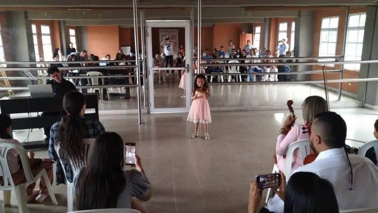 Une fille joue du violon lors d'un événement culturel pour enfants dans une salle avec des participants enregistrant sur leurs téléphones portables.