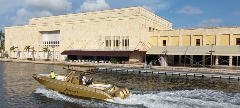 Barco de lujo navegando cerca del edificio histórico en un río, con los empleados disfrutando de un recorrido en un ambiente elegante y exclusivo en Colombia.