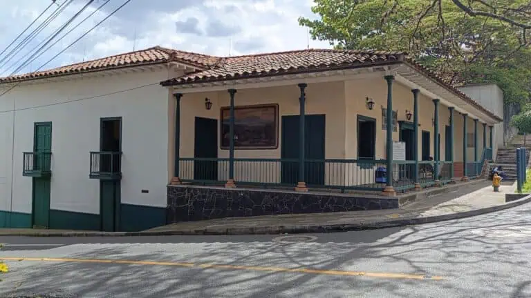 Centro cultural e de eventos em área urbana da Colômbia, fachada em estilo colonial, paredes brancas, portas e janelas verdes, terraço com parapeito, ambiente tranquilo, ideal para eventos e reuniões.
