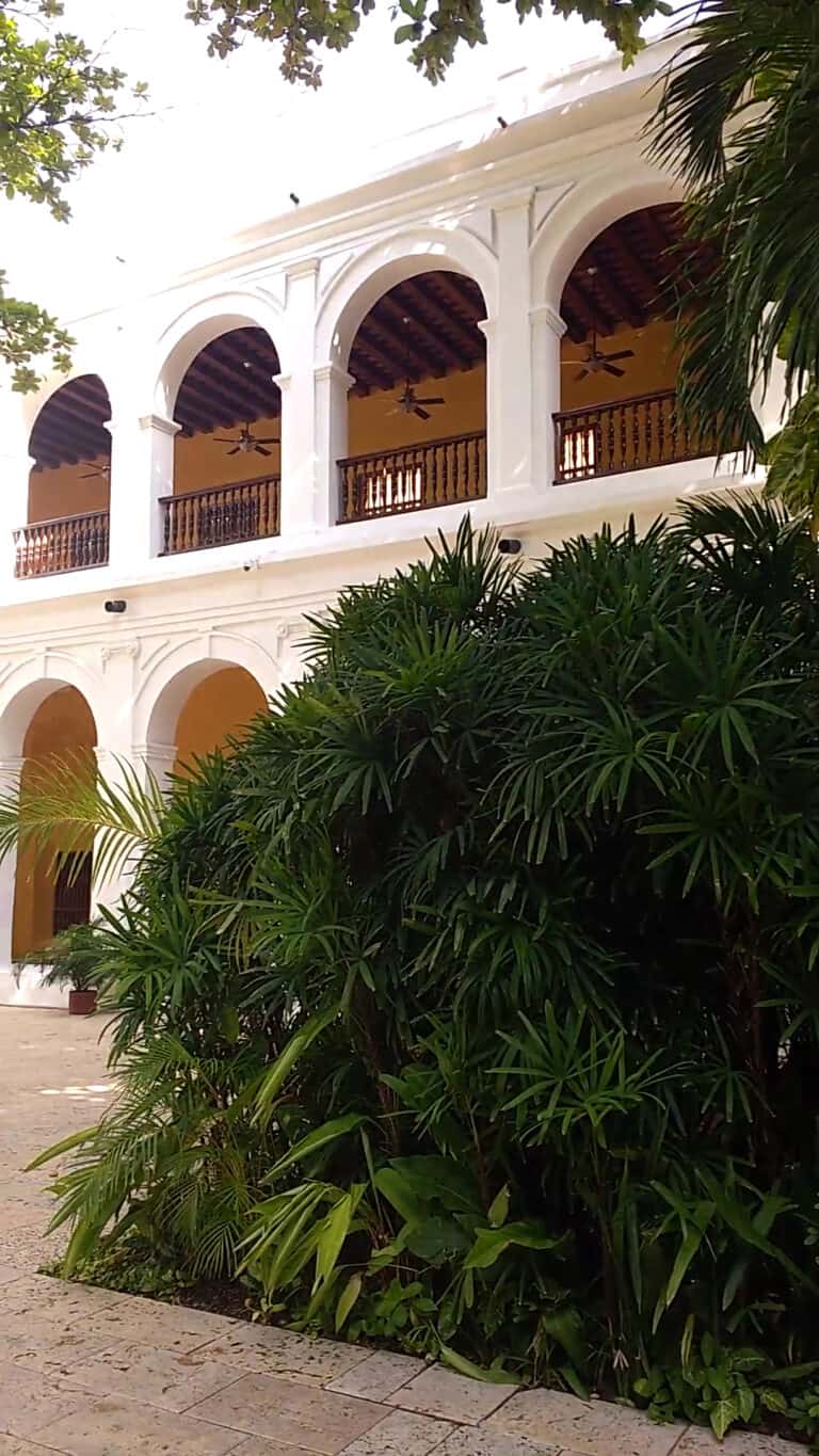 Casa colonial blanca con balcones de madera y techos de teja en un entorno tropical, rodeada de vegetación verde, ideal para eventos y reuniones al aire libre en Colombia.