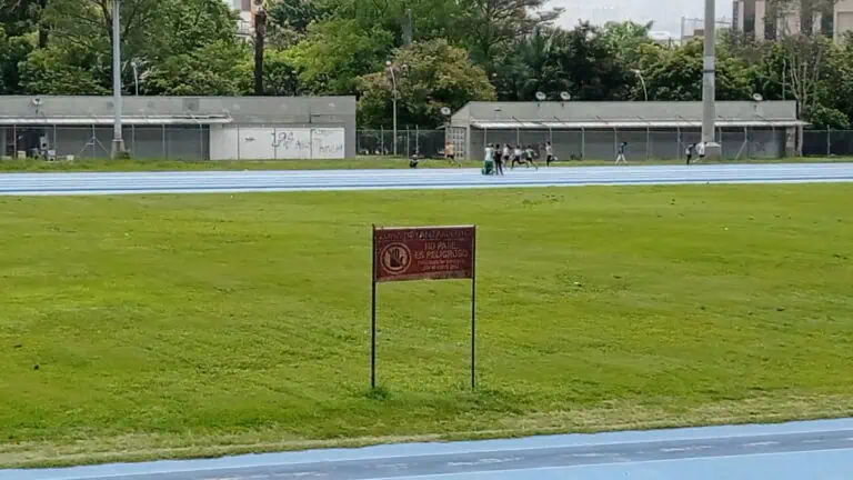 Boy on the running track of an outdoor stadium with a warning sign about the danger.