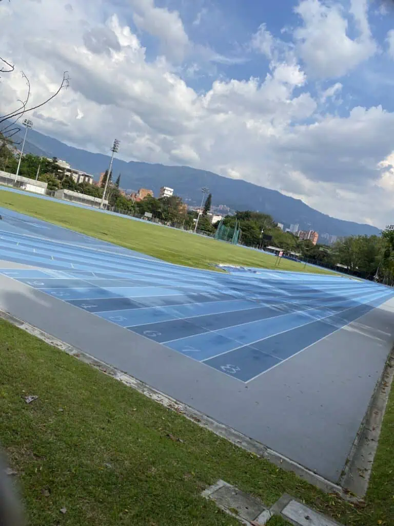 A blue athletics track in an outdoor stadium with a mountain backdrop and cloudy skies, ideal for sporting events and training in Colombia.