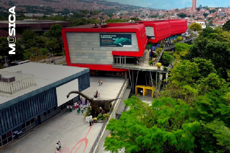 Disfruta del Museo de Ciencias Museo Museo en un edificio moderno de color rojo con vistas panorámicas de la ciudad y un dinosaurio de exhibición en el exterior.