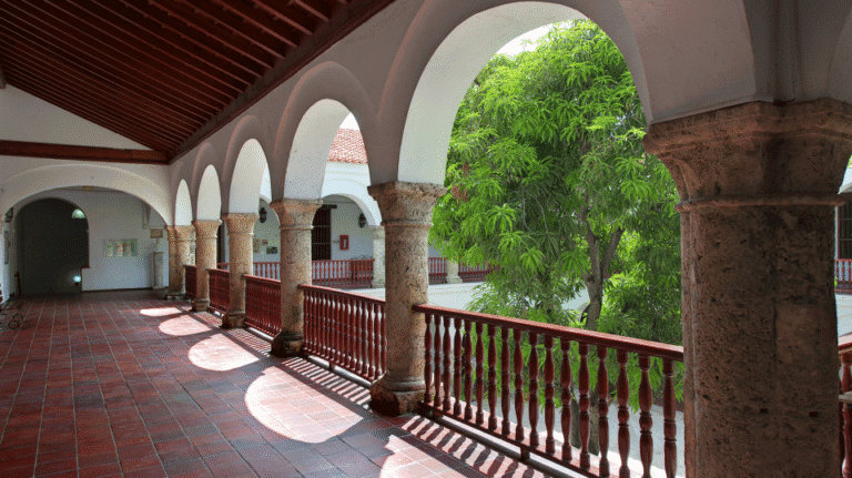 Sección del balcón del convento con arcos coloniales y vista a un árbol con follaje verde, espacio perfecto para eventos y reuniones en un ambiente histórico y natural.
