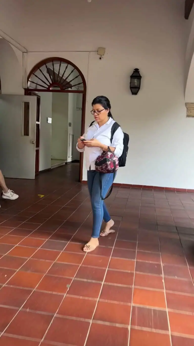 Frau in Turnschuhen und Rucksack benutzt ihr Mobiltelefon in einem Innenraum mit rotem Keramikboden bei einer Networking-Veranstaltung oder Konferenz.