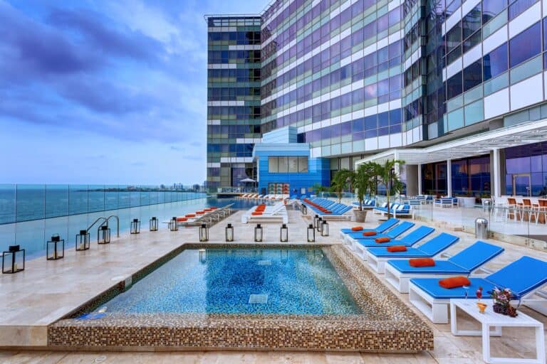 Piscina en azotea de hotel de lujo con vista al mar en la ciudad, áreas de descanso con tumbonas y sombrillas, ambiente moderno y elegante, ideal para eventos y relajación.