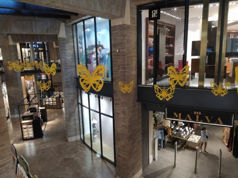 Diseño interior de centro comercial con tiendas y decoraciones de mariposas doradas para eventos y promociones en Colombia.