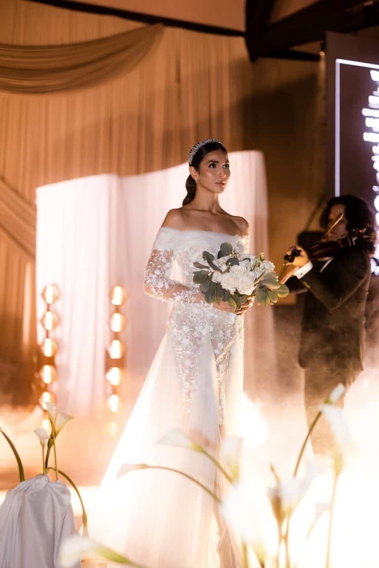 Vestido de novia de encaje blanco con details elegantes, bouquet de flores blancas y estilo sofisticado, en evento nupcial organizado por Eventario en Colombia, con ambientación y producción de alta calidad.