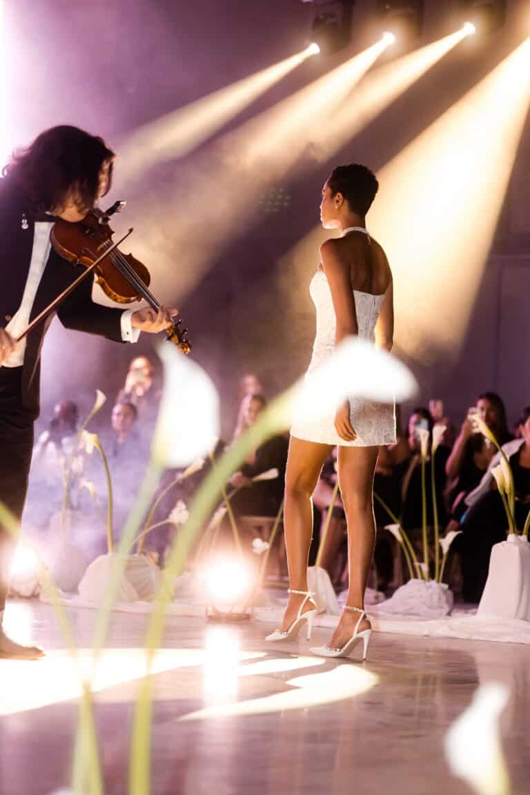 Bailarina en vestido blanco en un evento musical con orquesta en un entorno elegante y lleno de iluminación dramática.