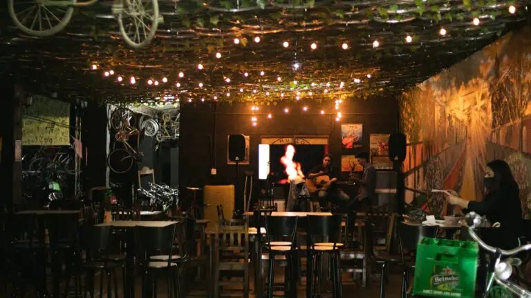 在装饰性照明的天花板下，酒吧里的音乐厅里，音乐家们正在现场弹奏吉他，气氛温馨舒适，墙壁上装饰着都市艺术，观众们正在欣赏现场音乐，夜色笼罩着一切。