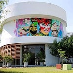 Colorido mural artístico en edificio moderno, foco en cultura y eventos con decoración vibrante y esculturas en un espacio al aire libre en Colombia.