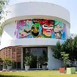 Farbenfrohes künstlerisches Wandgemälde an einem modernen Gebäude mit Schwerpunkt auf Kultur und Veranstaltungen mit lebendigem Dekor und Skulpturen in einem Außenbereich in Kolumbien.