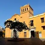 位于卡塔赫纳历史中心的殖民时期大教堂，拥有黄色的外墙、塔楼和前景中的树木，是哥伦比亚举办文化和旅游活动的理想场所。