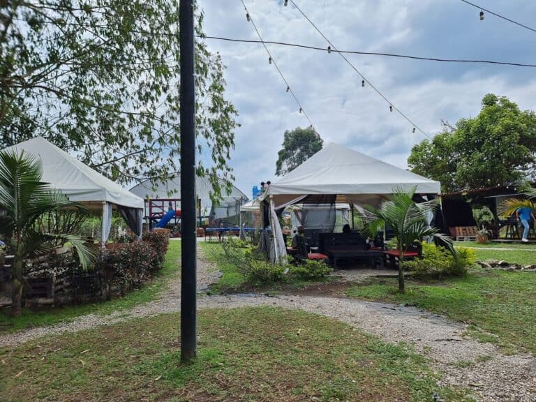 Toldos blancos en evento al aire libre con áreas de descanso y juegos para niños, rodeado de vegetación y luz cálida de ambiente, ideal para eventos y celebraciones en espacios naturales en Colombia.