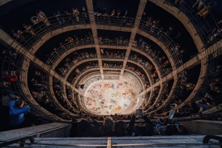 Espectáculo en un teatro con una vista panorámica del escenario desde arriba, rodeado de múltiples niveles con público asistente disfrutando del evento.