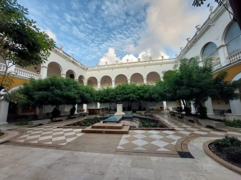 Amplio patio interior de edificio colonial con árboles verdes, fuente central y arcos tradicionales, ideal para eventos y reuniones sociales en un entorno histórico y elegante en Colombia.