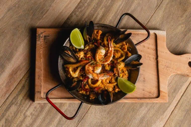 Riz aux fruits de mer avec fruits de mer et calamars, servi dans une poêle avec des citrons, idéal pour les événements et les célébrations, présenté sur une planche en bois pour de jolies photos.