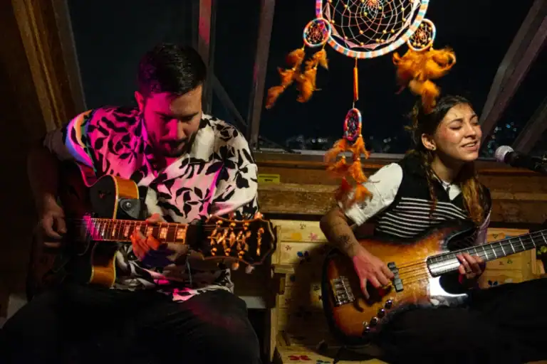 Artesanos interpretando música en un ambiente íntimo con decoración bohemia y atrapasueños en el fondo, ideal para eventos culturales y musicales en Colombia.
