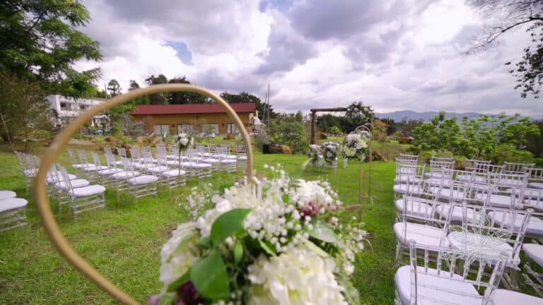 Arreglo floral en ceremonia al aire libre, decoración de boda en jardín con sillas blancas, evento en naturaleza, ideales para eventos y bodas con ambiente natural y elegante.
