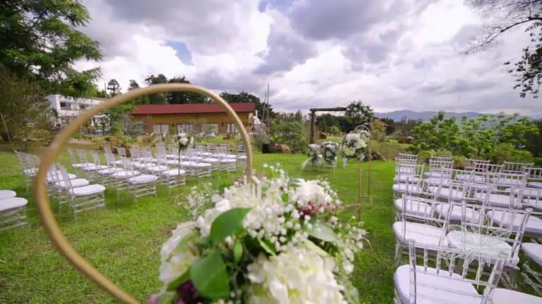 Blumenarrangement für eine Zeremonie im Freien, Gartenhochzeitsdekor mit weißen Stühlen, ein Naturereignis, ideal für Veranstaltungen und Hochzeiten mit einer natürlichen und eleganten Atmosphäre.