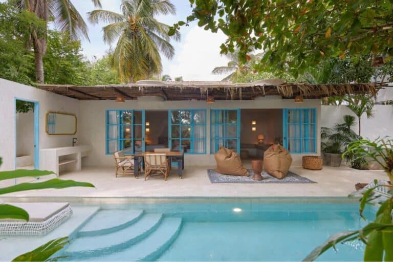 Vista de una casa en un entorno tropical con piscina, mobiliario rústico y vegetación abundante, ideal para eventos y alojamientos exclusivos en la costa.