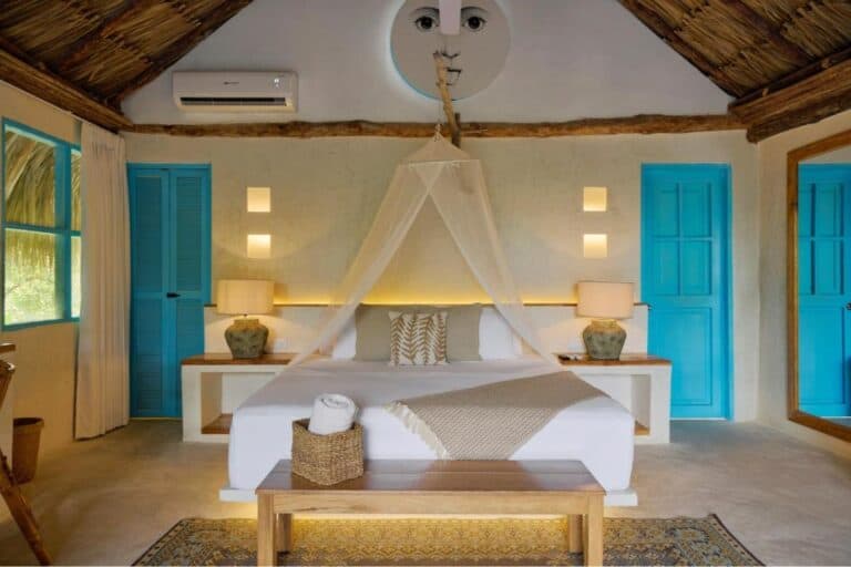 Relajante habitación con estilo tropical, cama con dosel y puertas azules, decorada con lámparas y detalles naturales, ideal para eventos y experiencias únicas en destinos exóticos en Colombia.