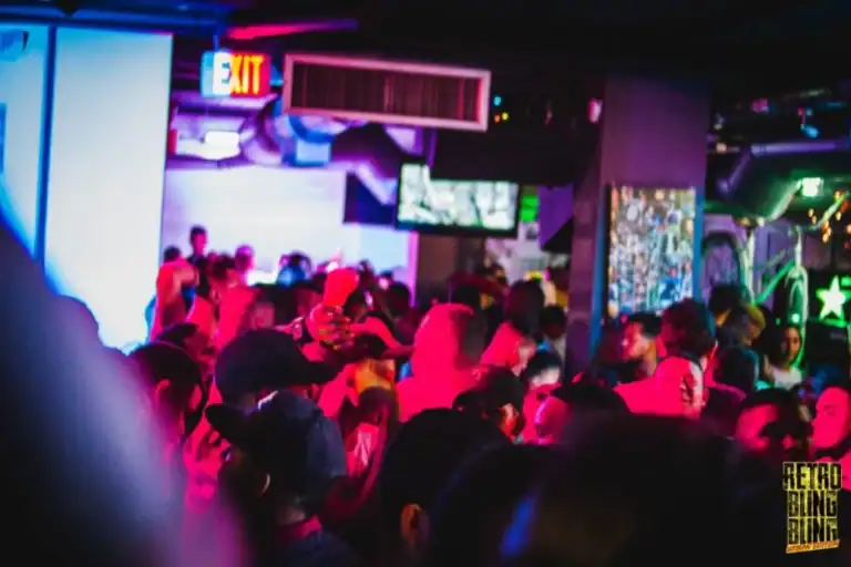 Diversidad de asistentes bailando en un evento nocturno con luces neón y ambiente festivo en un club o bar en Colombia.