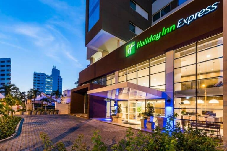 Holiday Inn Express frente al edificio, hotel moderno y elegante en zona urbana, con iluminación nocturna, plantas decorativas, y entorno de alta calidad para eventos y alojamiento en la ciudad.
