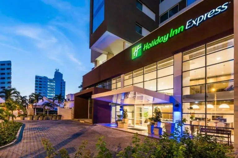 Holiday Inn Express across the street, a modern and elegant hotel in an urban area, with nighttime lighting, decorative plants, and a high-quality setting for events and accommodations in the city.