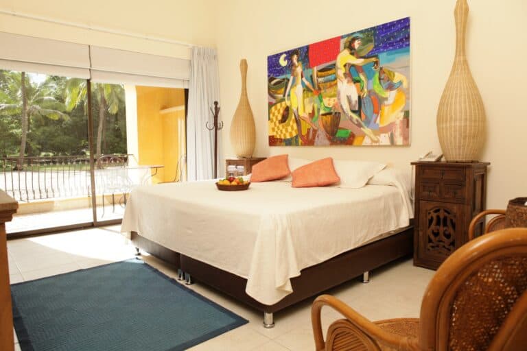 Relajante habitación con balcón y vista a área verde en un hotel boutique en Colombia. Decoración con arte vibrante, muebles en madera natural y ambiente acogedor. Ideal para descanso y eventos exclusivos.