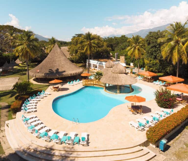 Cabañas y piscinas en un resort tropical con palmeras, áreas de descanso y vista a montañas, ideal para eventos y vacaciones en Colombia.