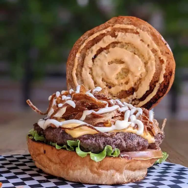 Gourmet sandwich met vlees, kaas, ui, spek en machinaal gebakken brood met een kaneelbroodje op een natuurlijke achtergrond.