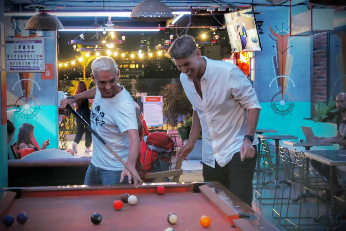 Divertida partida de billar entre amigos en un bar con ambiente vibrante y luces coloridas en la noche. Personas disfrutando de un momento social, risas y buena compañía.