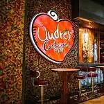 卡塔赫纳一家餐厅，醒目的霓虹灯招牌上写着“Qudes”。餐厅内部温馨舒适，装饰充满活力，吧台桌椅营造出热闹现代的氛围。