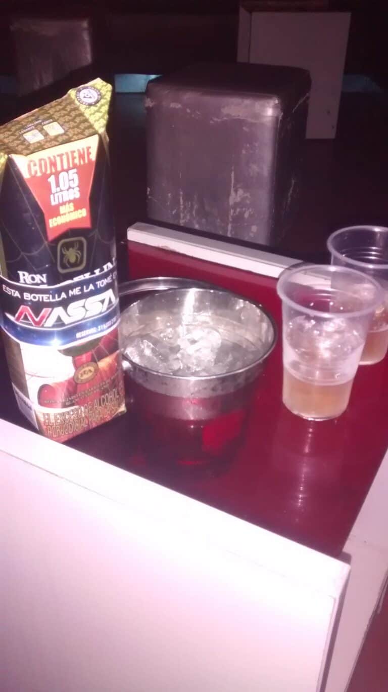 Botella de licor y vasos con bebidas en una mesa, promocionando bebidas alcohólicas para eventos y fiestas.