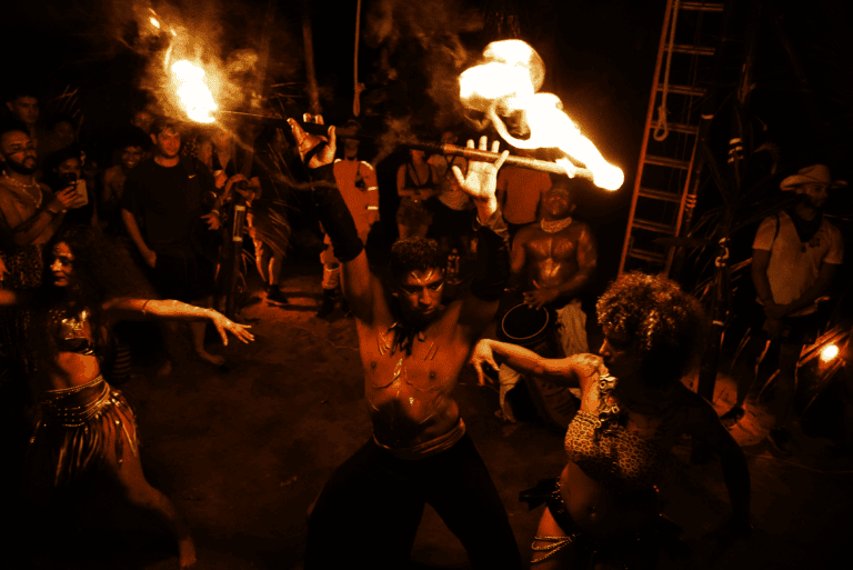 Espectáculo de fuego y danza en evento cultural colombiano con artistas en vestuarios coloridos y efectos de fuego, en un ambiente nocturno lleno de público disfrutando de la tradición artística.