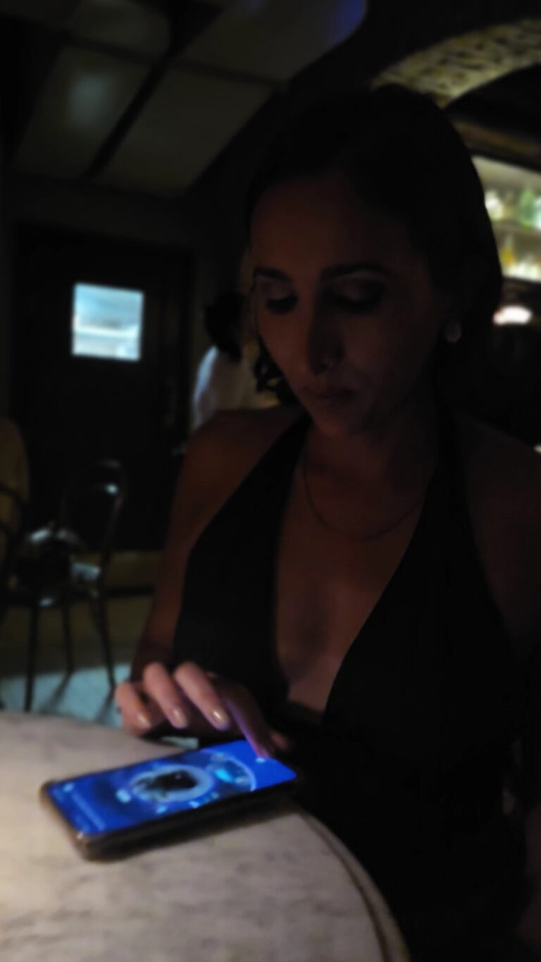 Mujer usando teléfono móvil en un ambiente con poca luz, participando en un evento o reunión profesional en Colombia.